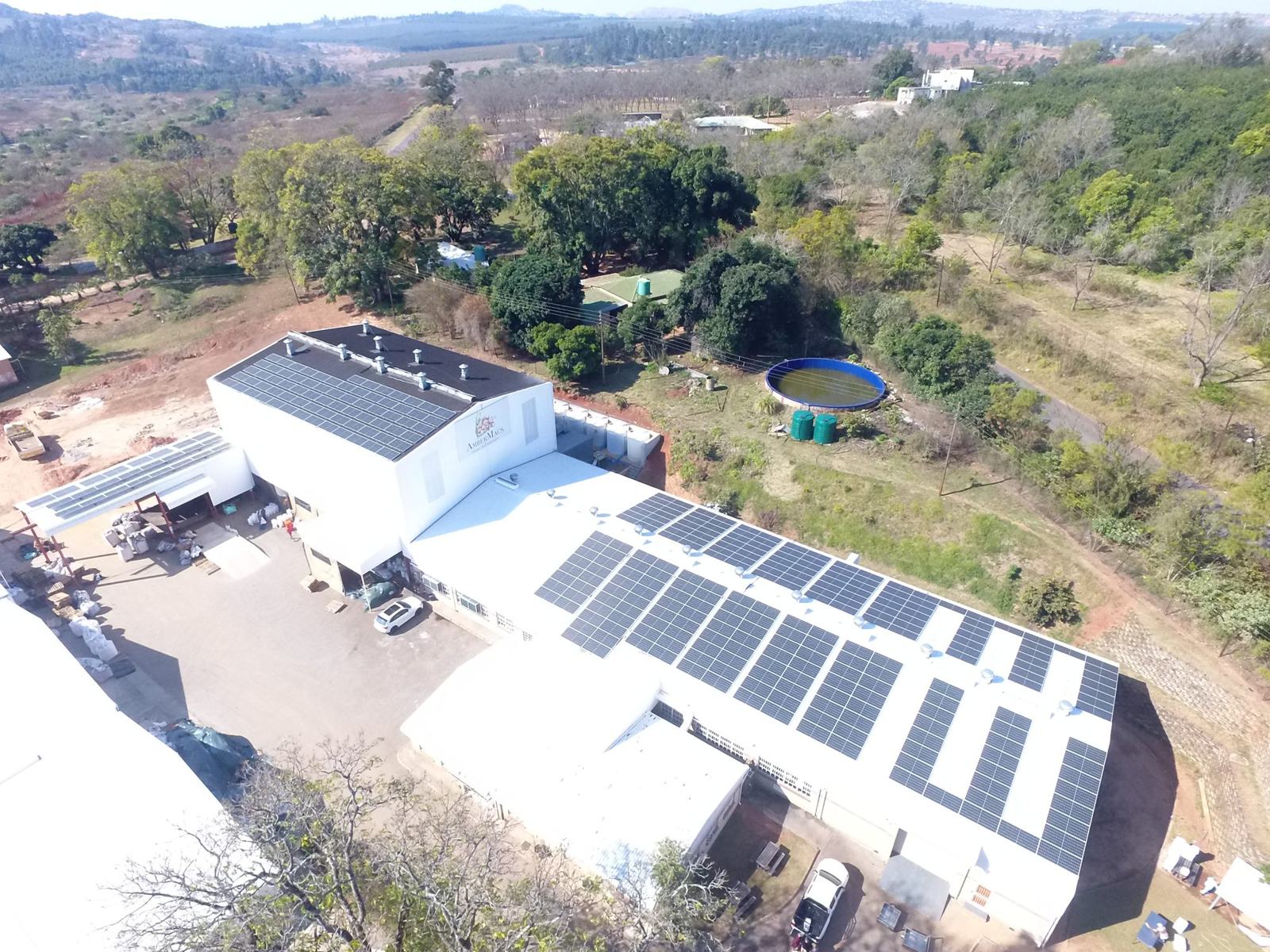 Aerial view of the Amber Macs factory with solar panels covering the roofs, surrounded by bush and orchards