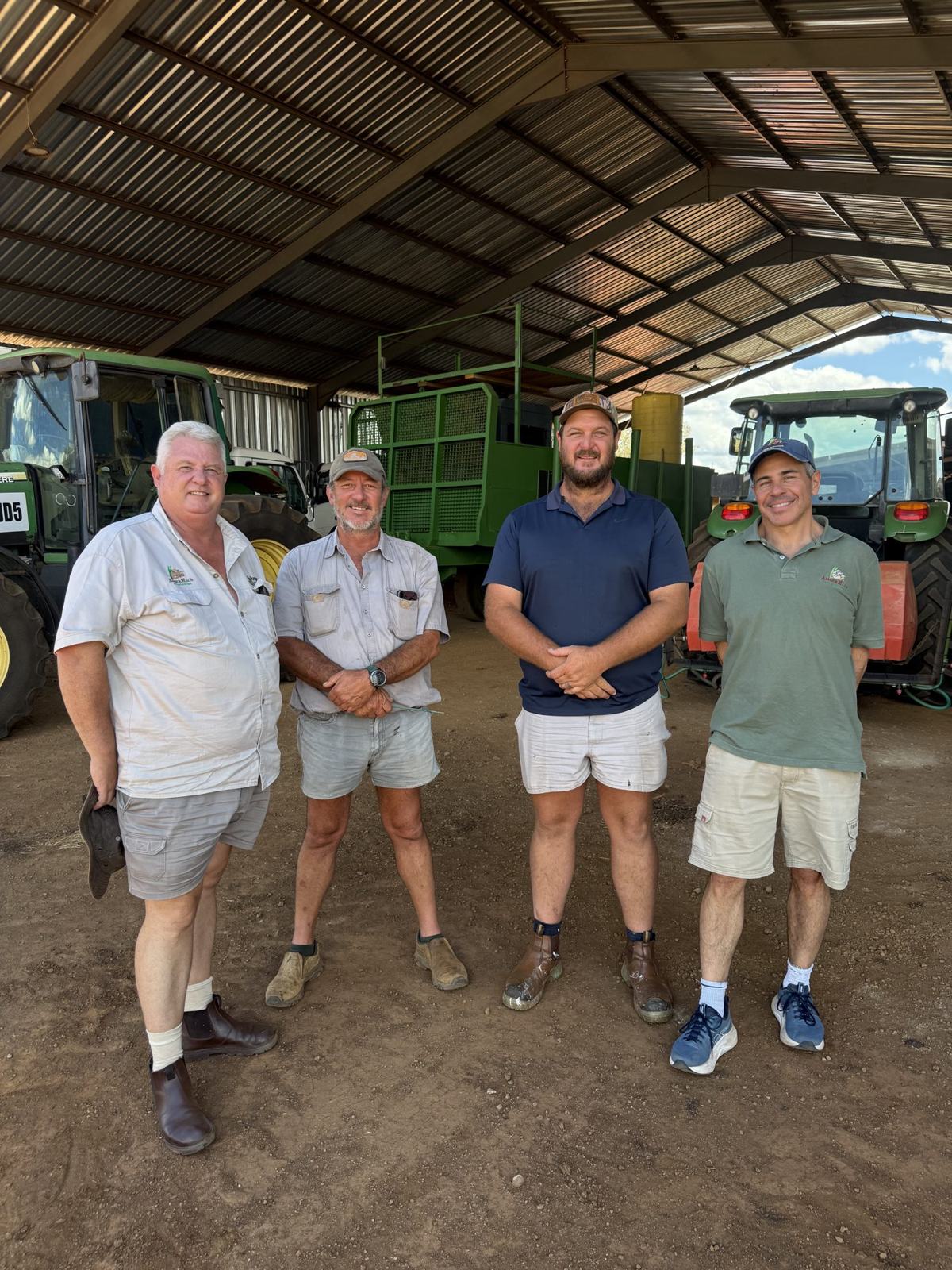 Four men standing in a farm shed in front of green tractors