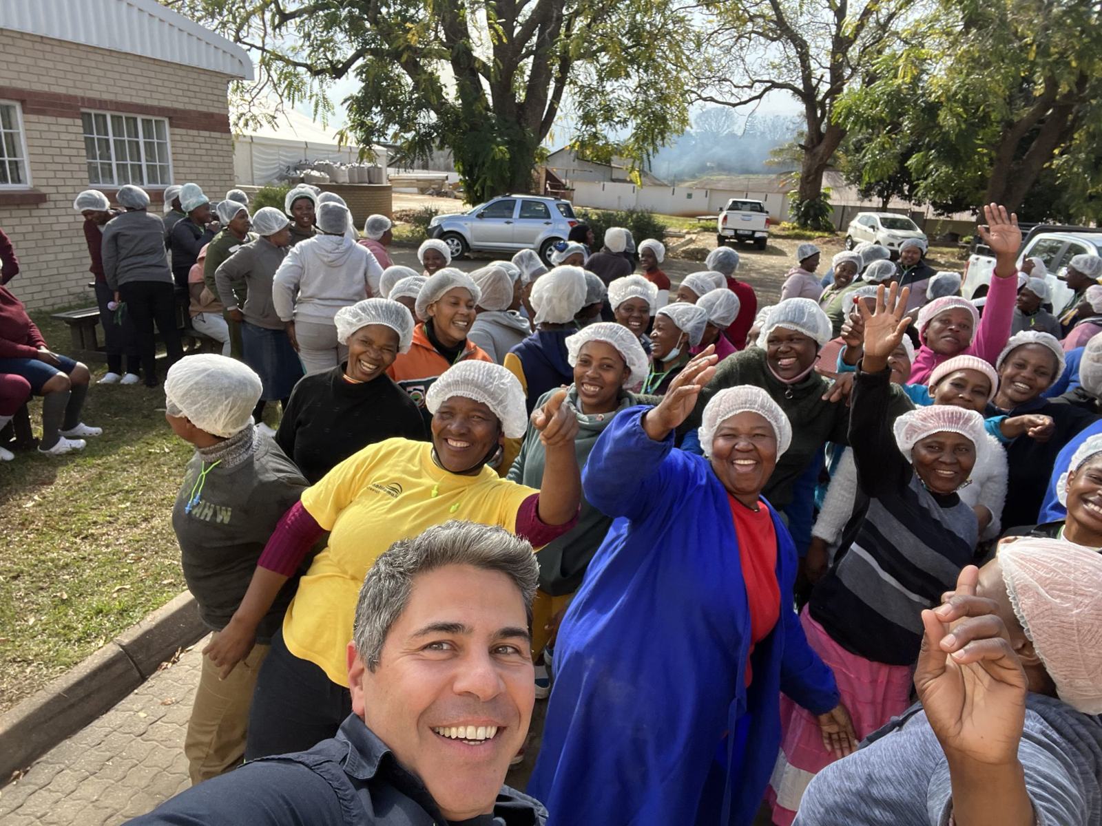 A large group of factory staff waving and smiling outside the factory